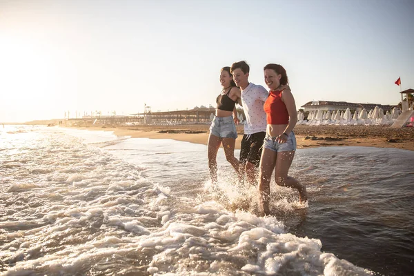 Three siblings enjoy their vacation by the sea and run into the sea at sunset.