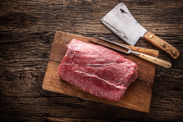 Raw rib eye steak whole on a wooden board with fork and chopping knife - Top of view.