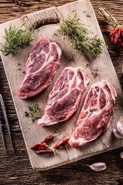Three sliced pieces of pork neck with herbs, chili spices and garlic on a cutting board.
