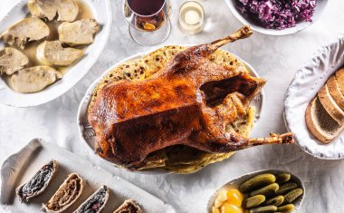 Roast goose with side dishes, red cabbage, roast, strudel, potato dumplings, pickles, bread and red wine. Traditional holiday food. Top view.