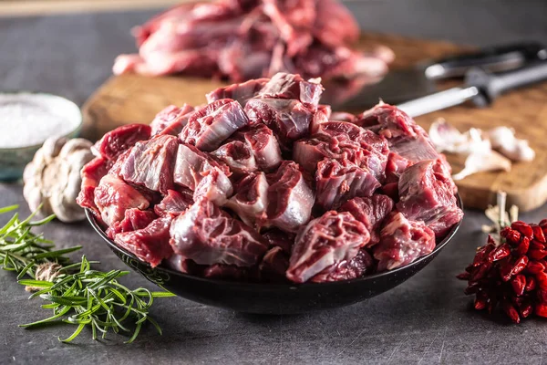 Fresh beef shank cuts piled in a bowl on a dark surface with herbs and spices around.