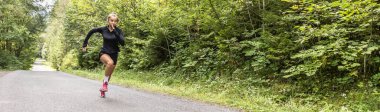 Banner of a female sprinter running throught the forest in the summer.