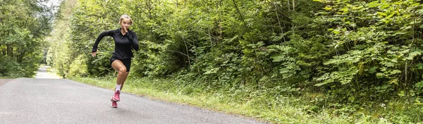 Banner of a female sprinter running throught the forest in the summer.