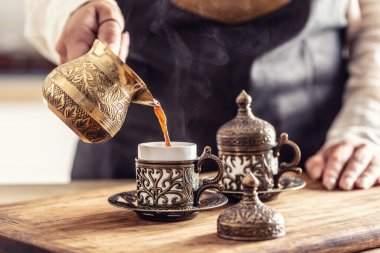 Traditional jezve coffee poured from ornamented copper pot into traditional mugs.