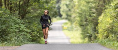Young female athlete runs up the hill on an asphalt road in the nature.