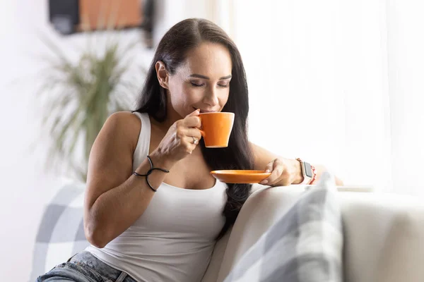 Woman smells fresh coffee from a mug in her hand having time for herself at home.