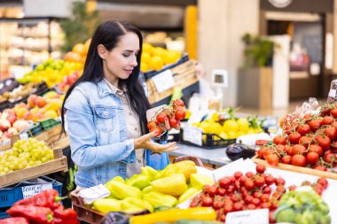 Gülümseyen güzel esmer, marketteki organik kırmızı domateslerin kalitesini ölçüyor..