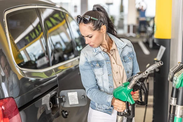 Woman holding gas and diesel pistols in the service station looks at the open gas tank of her car.