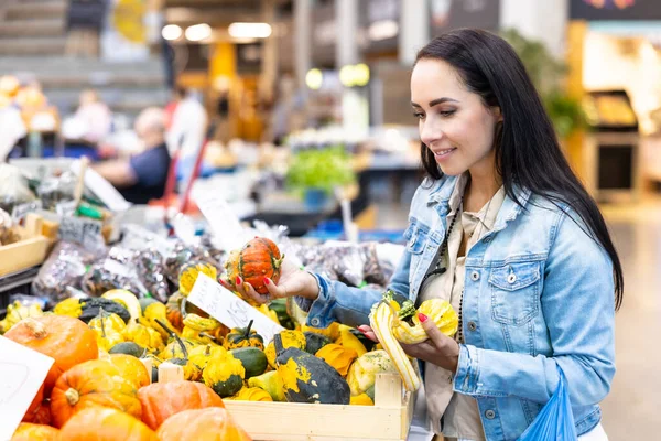 Smiling woman checks on pumpkins offered for sale in the grocery store.