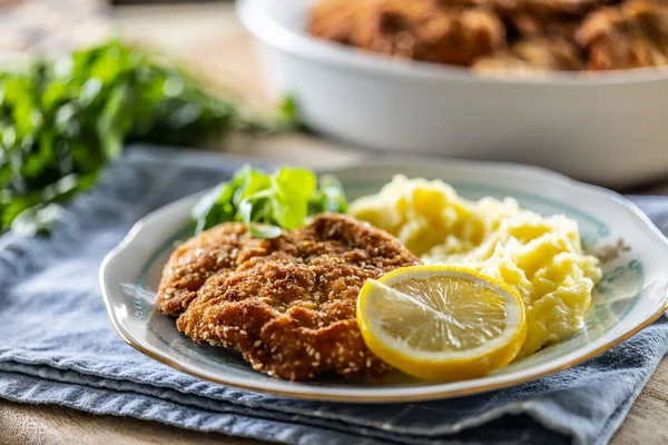 Breaded meat served with potato mash, slice of lemon and greens.