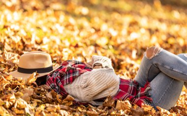 Genç bir kadın sıcak sonbahar günbatımında şapkayla kaplanmış, parkta uyuyor ya da dinleniyor..