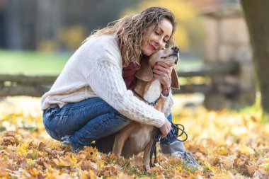 Genç bir kadın sonbahar parkında köpeğine sarılıyor..