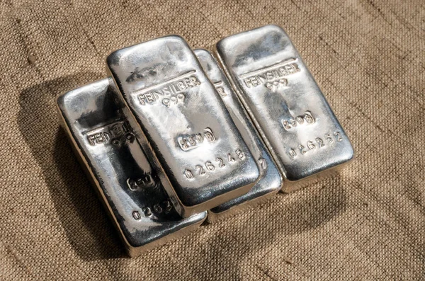 Four cast silver bars against the background of the texture of coarse cloth. feinsilber is fine silver.