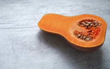 Çekirdekli, dikdörtgen kırmızı bir balkabağının yarısı mutfak masasında yatıyor..