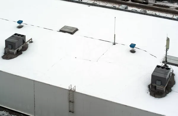 Roof of a commercial building with a external units of the commercial air conditioning and ventilation systems, cellular antenna and lightning rod. Winter photo