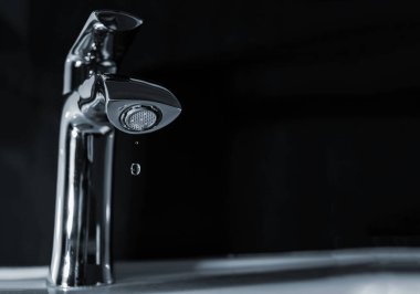 Musluktan damlayan bir damla saf su. Karanlık bir arka planda.