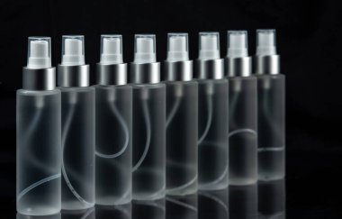 Siyah arka planda püskürtücü ile birlikte sıvı içeren saydam şişeler. Seçici odak.