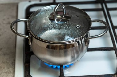 The water in a stainless steel pot is heated on a gas stove. clipart