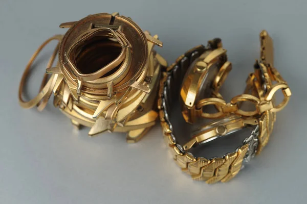 A bunch of old gold-plated watch cases and gold watches with bracelets. A scrap of gold on gray background.