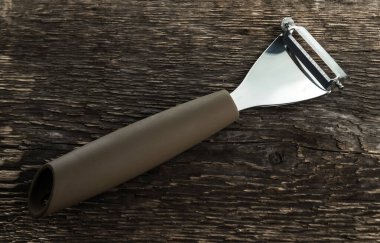 Kaba ahşap bir arka planda sebze ve meyve temizlemek için soyucu.