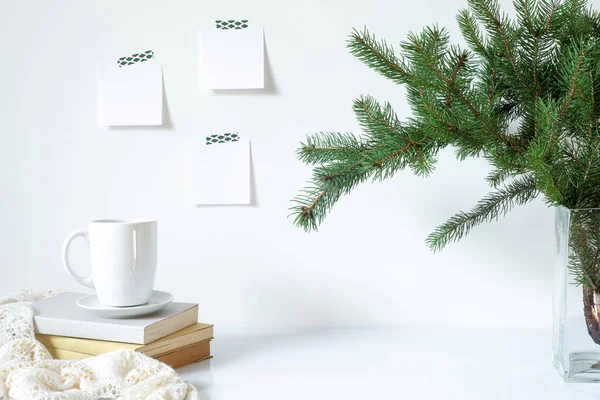 Şenlikli kahvaltı hala hayattadır. Bir fincan kahve, kitap ve vazo ve köknar dalları. Boş not defterleri beyaz duvara asılıdır. Noel süsü.