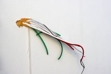 Beyaz, yeşil, kırmızı kablolar beyaz duvardan sarkıyor. Elektrik kabloları.