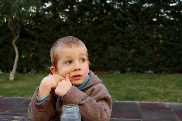 ブロンドの少年は 夢のように遠くを見て 口を開けています 4歳の男の子が彼の頬を手で小道具 — ストック写真