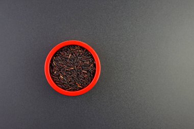 Gri arka planda yuvarlak kırmızı bir kase içinde siyah uzun tahıllı pirinç..