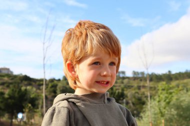 Sarışın çocuk cilveli bir şekilde gülümsüyor ve uzaklara bakıyor..