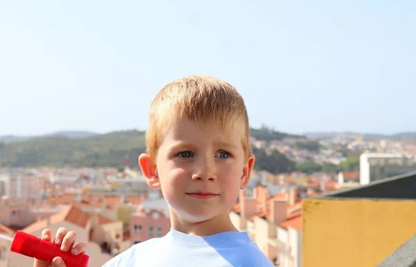 かわいい金髪の男の子は興味と笑顔で目を離しています オレンジの屋根を背景にした5歳の少年 — ストック写真