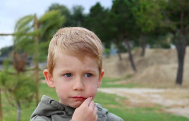 Ağzı bozuk ve ağzında kiraz olan sarışın bir çocuk. Düşünceli beş yaşındaki çocuk dışarıda meyve yiyor..