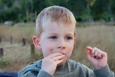 Sarışın çocuk bir ısırık alır ve gülümser. Mutlu beş yaşındakiler.