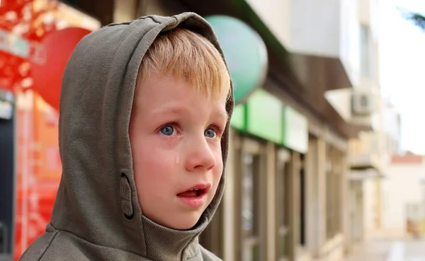 A hooded boy with a red face and a tear on his cheek. Sad five year old boy in tears.