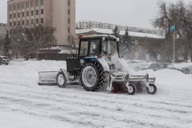 Uralsk, Kazakistan (Kazakistan), 11.03.2022 - Uralsk şehrinde bir traktörle kar temizleme, kovalı bir traktör ve kar temizleme fırçası, kaldırımdaki karı kaldıran bir traktör