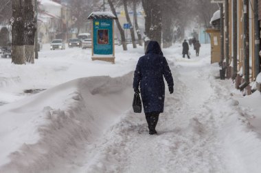 Uralsk, Kazakistan (Kazakistan), 11.03.2022 - kentte kar fırtınası, insanlar karlı bir kaldırımda yürüyor, şehirde kar yağıyor, bir kadın kar yağışı, tipi, kar yağışı