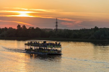 Şehir parkında gün batımında Uralsk şehrinde nehir tramvayı var. İnsanlarla dolu nehir feribotu gün batımında nehirde yüzer.