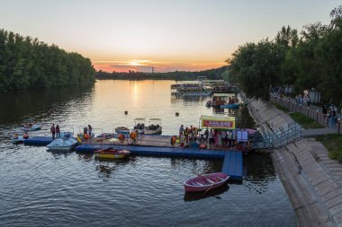 Uralsk, Kazakistan (Kazakistan), 8.07.2022 - Uralsk kentinin kültür ve dinlenme parkındaki iskeledeki katamaranlar ve botlar. Gün batımında Chagan nehri