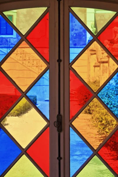 View through the stained glass window of a garden pavilion: formal garden path-trimmed hedges-metal railing staircase-south facing facade of a NeoRococo palace. Estoi parish-Faro-Algarve-Portugal.