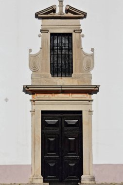 Rectangular wooden doorway surmounted by a closed lattice grating window with lateral pilasters-whitewashed front facade of Sao Lourenco-Saint Lawrence Church. Almancil parish-Loule-Algarve-Portugal.