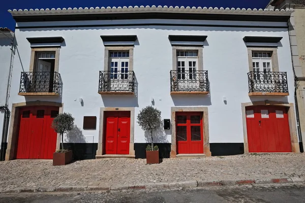 赤漆塗りの閉じたドアと石畳の歩道上に黒塗りの錬鉄手すりと4つの白いバルコニーが付いている有名な町家の白塗りのファサード タビラ アルガルヴェ地方 ポルトガル — ストック写真