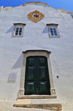 13. yüzyılın ana cephesi Saint James Kilisesi-Igreja Matriz de Sao Tiago 'yu yeniden inşa etti. Yeşil ahşap kapılı madalyon Santiago 'yu at sırtında tasvir ediyor. Tavira-Algarve-Portekiz.