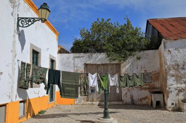 Güneşte kuruyan ve duvara asılmış bir çamaşır ipine asılan ve Rua Antonio Maria Laboia Str 'daki yeşil bir fıskiyeye dayanan eski bir aksesuar. Faro-Algarve-Portekiz.
