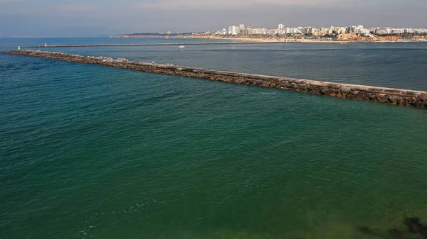 Portimao şehri ve Praia da Rocha Sahili 'nin panoramik manzarası Rio Arade Nehri' nin doğu tarafındaki uçurumlardan dış limanı koruyan köstebeklerin karşısından. Ferragudo-Algarve-Portekiz.