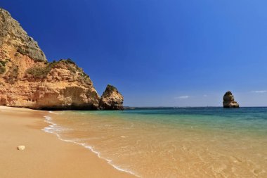 Praia do Camilo Plajı 'nın kuzey bölümünü çevreleyen aşınmış kayalıklar ve kumtaşı kireçtaşı kaya yığınları yüzerek kıyıdan geçen deniz kanoları. Lagos-Algarve-Portekiz.