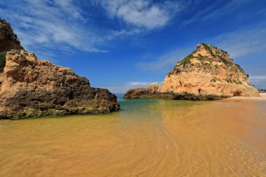 Büyük Praia do Alvor Beach-Lagos şehrinin Praia dos Tres Irmaos Sahili 'nin en doğusundaki deniz yığınları arasında gelgit havuzu üzerinden batıya doğru görünüyor. Alvor Portimao-Algarve-Portekiz.