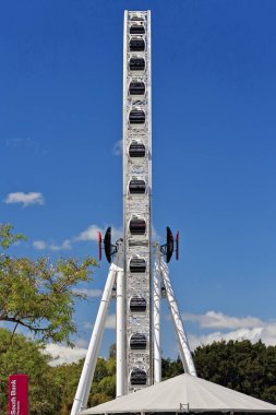 Dönme dolap, temiz mavi gökyüzüne ve CBD-Merkezi İş Bölgesi 'nin karşısındaki South Bank Parklands bölgesinde beyaz bulutlara karşı profilde görünüyor. Brisbane-Queensland-Avustralya.