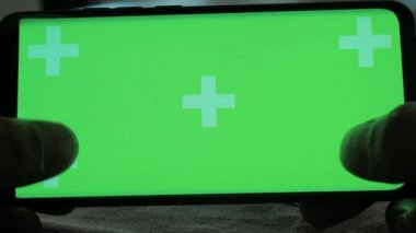 Yeşil ekranlı telefon, akıllı telefondan oyun oynayan bir adamın ellerinde.