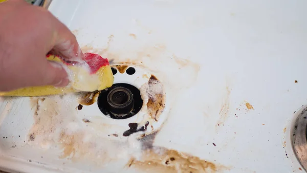 Close-up van een mans handen die het oppervlak van een modern gasfornuis in de keuken schoonmaken met een spons. Wassen en reinigen wandtegels en keukenfornuis van vet — Stockfoto