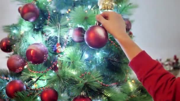Χαρούμενο χέρι μωρού κρέμεται μπάλα σε ένα χριστουγεννιάτικο δέντρο, τα παιδιά διακοσμούν ένα χριστουγεννιάτικο δέντρο. — Αρχείο Βίντεο
