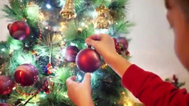 Mutlu küçük çocuk Noel ağacını toplarla süslüyor..